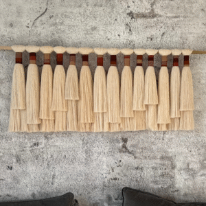 Handmade neutral fiber wall hanging titled 'Horizon' with layered cream and brown cotton fringe on a wooden dowel, displayed against a light background