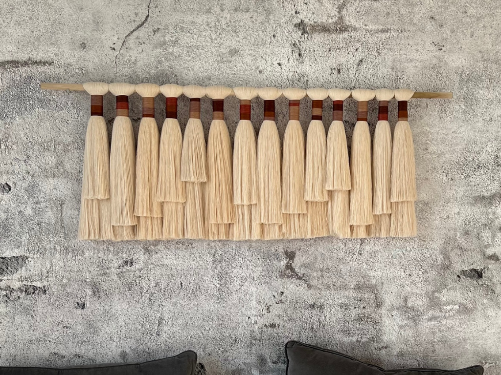 Handmade neutral fiber wall hanging titled 'Horizon' with layered cream and brown cotton fringe on a wooden dowel, displayed against a light background